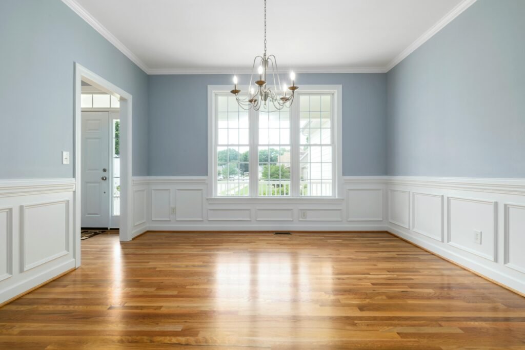 Bright empty room featuring a chandelier, wooden floor, and large windows.